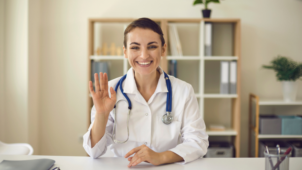 Nurse smiling and waving sat at her desk.